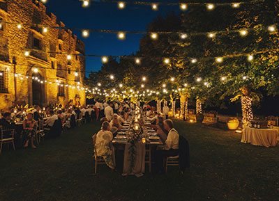 allestimento con filari di lampadine luminosee tavola con aprtecipanti ad una cena