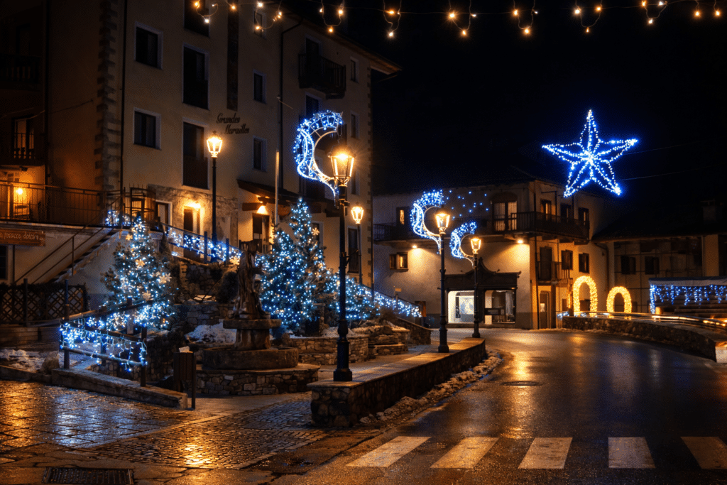 Una strada di paese illuminata a festa di notte, con alberi decorati con luci blu, lampioni e decorazioni a forma di stella e luna
