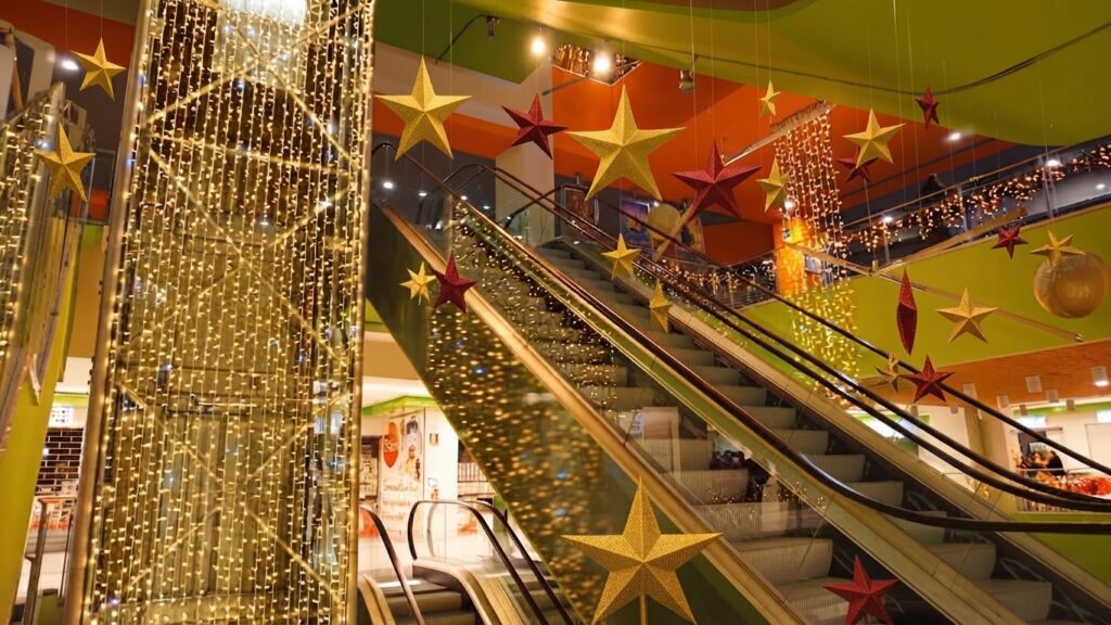 Scale mobili in un centro commerciale decorate a festa con grandi stelle dorate e rosse sospese e luci natalizie scintillanti